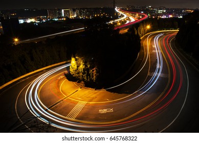 Car Driving Down A Winding Road At Night, Long Exposure Of Headlights An Taillights In Blurred Motion