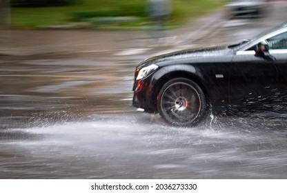 Car driving fast through big puddle at heavy rain, water splashing over the car. Car driving on asphalt road at heavy rain. Dangerous driving conditions. Dangers of aquaplaning. MOTION BLUR - Shutterstock ID 2036273330