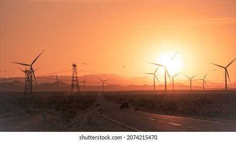 Car Driving Into Sunset With Windmills And Electricity Pylons. 