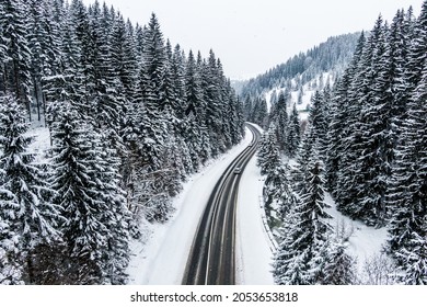 Car Driving On Asphalt Road Through The Winter Snowy Forest . Drone Top View Of Frozen Winter Forest. Areal View.