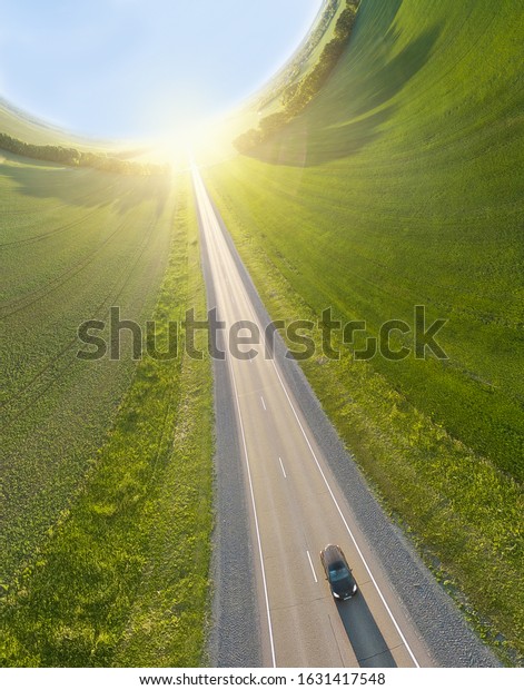 Car driving on the highway from the sun\
at sunset surrounded by fields with green\
grass