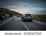 A car driving on a quiet mountain road during twilight, surrounded by rolling hills and a serene sky, evoking a peaceful road trip experience.