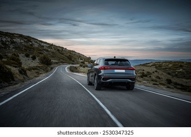 A car driving on a quiet mountain road during twilight, surrounded by rolling hills and a serene sky, evoking a peaceful road trip experience.