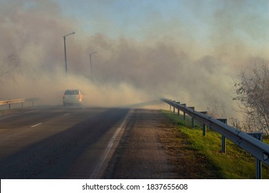 A Car Driving On A Suburban Highway During A Fire On The Side Of The Road In Strong Smoke