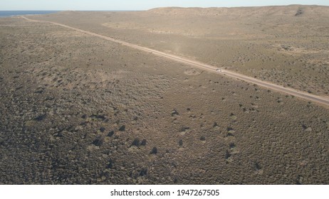 Car Driving Over Rural Road In The Australian Desert With A Long Shadow During Golden Hour In Exmouth, Western Australia. Angle Aerial Drone Shot