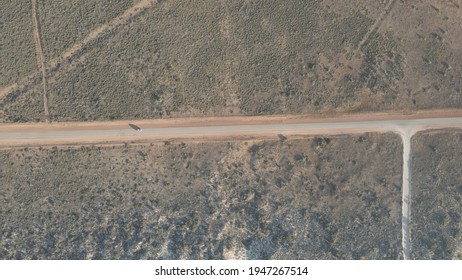 Car Driving Over Rural Road In The Australian Desert With A Long Shadow During Golden Hour In Exmouth, Western Australia. Top Aerial Shot