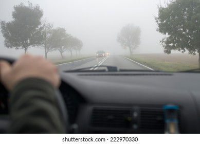 Car Driving In Thick Fog, Seen Through Windscreen Of Other Vehicle