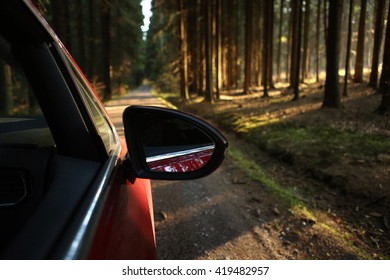 Car Driving Through The Forest On A Sunny Road At Sunset In The Woods Viewed From Outside Passenger Window With Sun Pouring Through Trees On An Open Road With No People