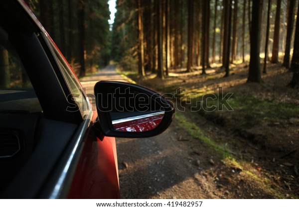 Car driving through the\
forest on a sunny road at sunset in the woods viewed from outside\
passenger window with sun pouring through trees on an open road\
with no people