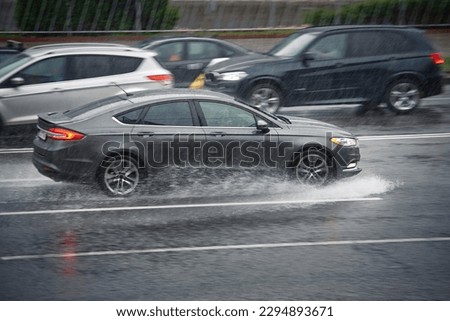 Car driving through puddle at heavy rain, water splashing over car. Car driving on flooded asphalt road at heavy rain, wet road. Dangerous driving conditions, risk of aquaplaning. MOTION BLUR.