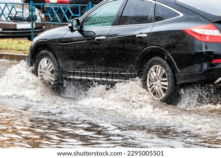 The car is driving through a puddle in heavy rain. Splashes of water from under the wheels of a car. Flooding and high water in the city