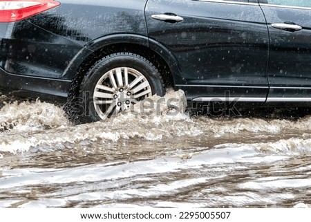 The car is driving through a puddle in heavy rain. Splashes of water from under the wheels of a car. Flooding and high water in the city