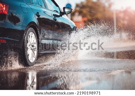 Car driving through the puddle and splashing by water.