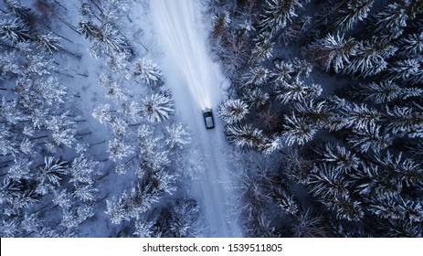 Car Driving Through The Winter Snowy Forest On Country Road At Night. Top Down View.