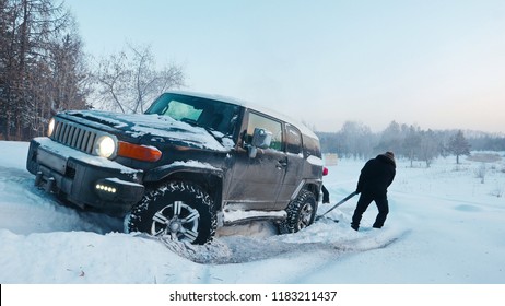 Car Driving Through A Winter Storm With Snow On A Forested Road. Black SUV  Sticks In Deep Snow Slips.