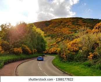 Car Driving In UK On Left Side Of Winding Road Toward Mountain Into Sunset