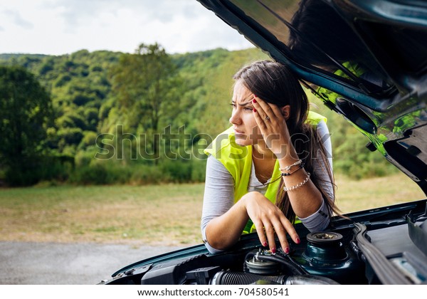 Car engine broke down and white\
young female is desperately waiting for auto repair service\
