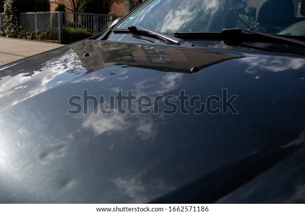 Car engine hood with many hail damage dents show\
the forces of nature and the importance of car insurance and a\
replacement value insurance against stormy weather and storm\
hazards or extreme weather