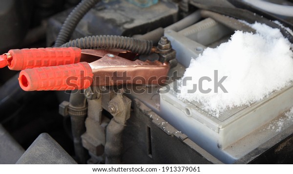 Car engine starting wire red crocodile terminal on\
frozen snowy car battery + pin close up, Quick start vehicle engine\
on a winter frost 