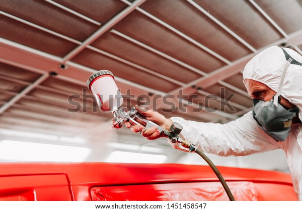 car engineer and auto mechanic\
working and painting a red car using spray gun and\
compressor