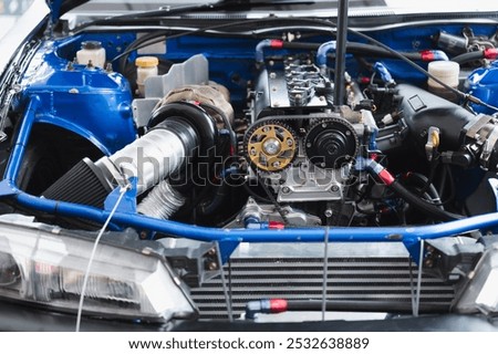 Car enthusiasts inspect an engine in a modified car as another engine powers a vehicle with turbo upgrades for the industry and aftermarket diy systems, featuring design, horsepower, technology, art, blue innovation, speed, and community.