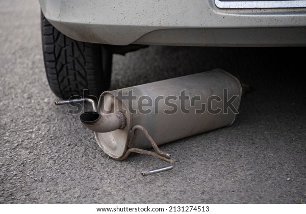 Car exhaust, muffler fallen down on the\
ground in traffic road, left behind the car in background. Rusty\
chasis of a car. Damaged exhaust\
pipe.
