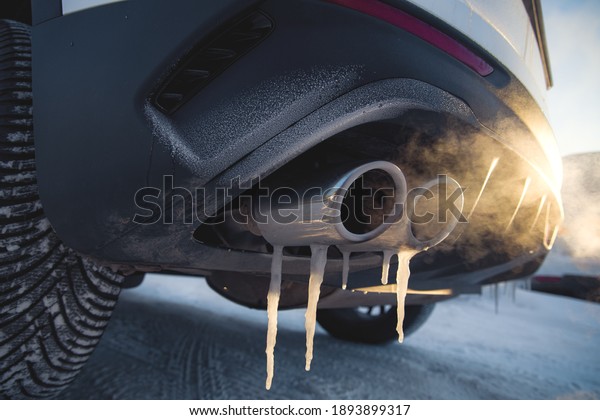 car exhaust pipe with icicle and smoke at\
shallow depth of field on a frosty\
day