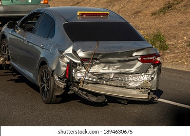 A Car With Extensive Rear End Damage Being Towed On A Freeway