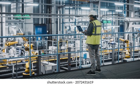 Car Factory Engineer in High Visibility Vest Using Laptop Computer. Automotive Industrial Manufacturing Facility Working on Vehicle Production with Robotic Arms Technology. Automated Assembly Plant. - Shutterstock ID 2072431619