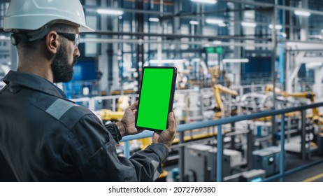 Car Factory Engineer In Work Uniform Using Tablet Computer With Green Screen Mockup Display. Augmented Reality Software At Automotive Industrial Manufacturing Facility Working On Vehicle Production.