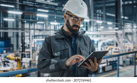 Car Factory Engineer In Work Uniform Using Tablet Computer. Automotive Industrial Manufacturing Facility Working On Vehicle Production With Robotic Arms Technology. Automated Assembly Plant.