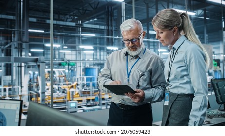 Car Factory: Female Project Manager Talks To Male Automotive Engineer, Plan Strategy Using Tablet Computer. Automated Robot Arm Assembly Line Production Conveyor Manufacturing Electric Vehicles