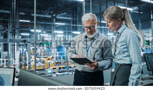 Car Factory: Female Project Manager Talks to\
Male Automotive Engineer, Plan Strategy Using Tablet Computer.\
Automated Robot Arm Assembly Line Production Conveyor Manufacturing\
Electric Vehicles