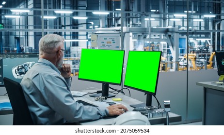 Car Factory Monitoring Office: Male Chief Automotive Engineer Sitting At The Desk Working On Green Screen Chroma Key Computer. Automated Robot Arm Assembly Line Manufacturing Vehicles