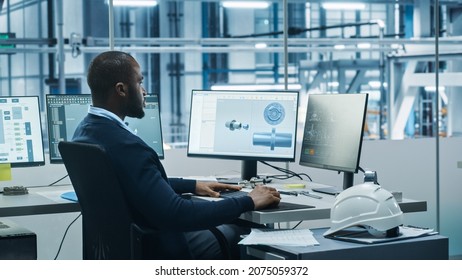 Car Factory Office: Black Engineer Working On Desktop Computer, Screens Show CAD Software With 3D Component, Monitoring Of Automated Robot Arm Assembly Line Manufacturing High-Tech Electric Vehicles