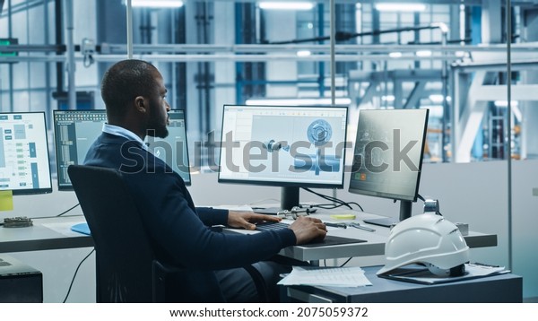 Car Factory Office: Black Engineer Working on\
Desktop Computer, Screens Show CAD Software with 3D Component,\
Monitoring of Automated Robot Arm Assembly Line Manufacturing\
High-Tech Electric Vehicles