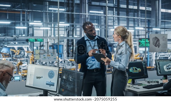 Car Factory Office: Female Engineer Talks with\
Male Scientist, Use Tablet Computer to Design Production Conveyor\
for Advanced Power Engines. Automated Robot Arm Assembly Line\
Manufacturing Vehicles