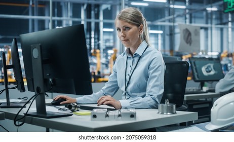 Car Factory Office: Portrait Of Confident Female Chief Engineer Working On Desktop Computer. Professional Technician In Automated Robot Arm Assembly Line Manufacturing High-Tech Electric Vehicles