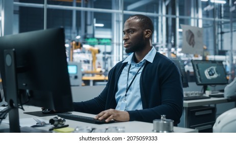 Car Factory Office: Portrait Of Confident Black Male Chief Engineer Working On Desktop Computer. Professional Technician In Automated Robot Arm Assembly Line Manufacturing High-Tech Electric Vehicles