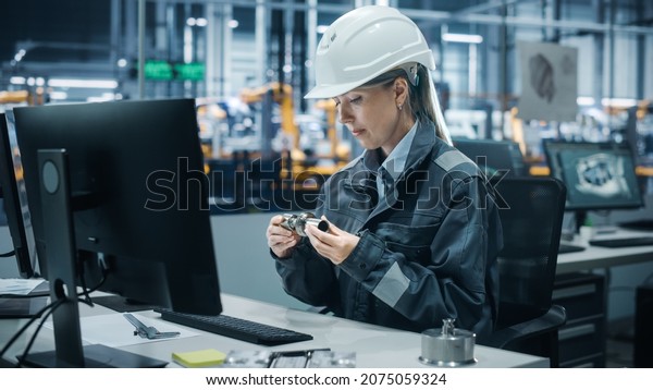 Car Factory Office: Portrait of Confident Female\
Chief Engineer Wearing Hard Hat Working on Desktop Computer.\
Technician in Automated Robot Arm Assembly Line Manufacturing\
High-Tech Electric Vehicles