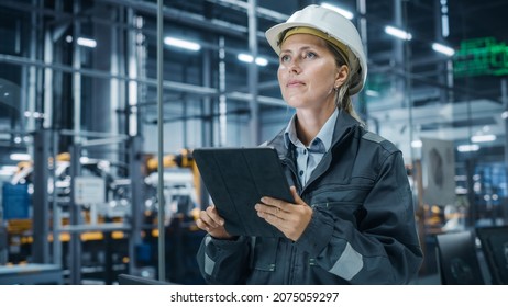 Car Factory Office: Portrait of Female Chief Engineer Wearing Hard Hat Monitoring Production Conveyor with Tablet Computer. Automated Robot Arm Assembly Line Manufacturing High-Tech Electric Vehicles - Powered by Shutterstock