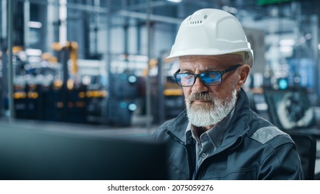 Car Factory Office: Portrait Of Male Engineer Working On Computer. Automated Robot Arm Assembly Line Manufacturing Electric Vehicles. Technician Monitoring Electronics Production. Close-up Shot