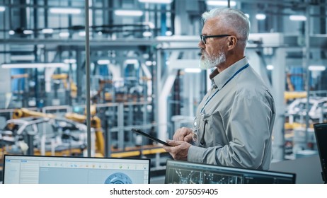 Car Factory Office: Portrait Of Senior White Male Chief Engineer Using Tablet Computer In Automated Robot Arm Assembly Line Manufacturing High-Tech Electric Vehicles. Side View Shot