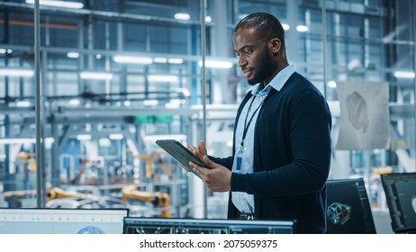 Car Factory Office: Portrait Of Successful Black Male Chief Engineer Using Tablet Computer In Automated Robot Arm Assembly Line Manufacturing High-Tech Electric Vehicles. Side View Shot