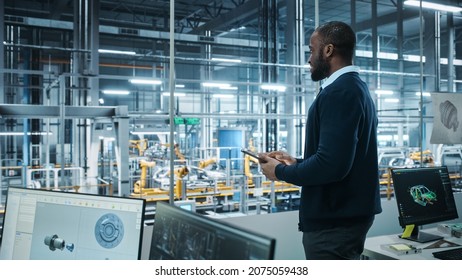 Car Factory Office: Portrait Of Successful Black Male Chief Engineer Using Tablet Computer In Automated Robot Arm Assembly Line Manufacturing High-Tech Electric Vehicles. Side View Shot