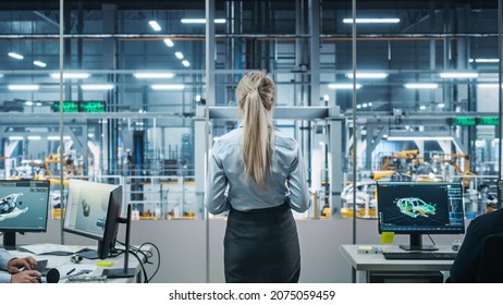 Car Factory Office: Successful Female Chief Engineer Overlooking Factory Production Conveyor. Automated Robot Arm Assembly Line Manufacturing Advanced High-Tech Electric Vehicles. Back View Shot