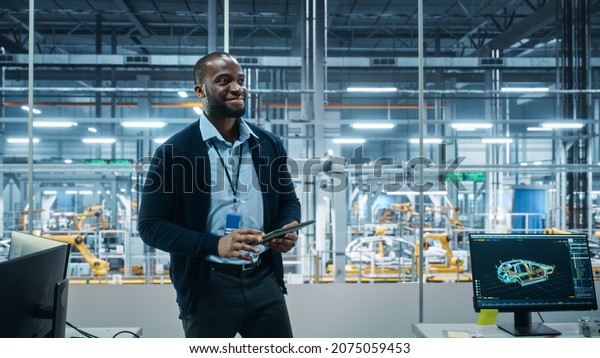 Car Factory Office: Successful Male Chief Engineer\
Overlooking Factory Production Conveyor. Automated Robot Arm\
Assembly Line Manufacturing Advanced High-Tech Electric Vehicles.\
Back View Shot