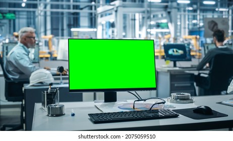 Car Factory: On the Desk Green Screen Chroma Key Computer. In Background Diverse Team of Engineers Work in Office of Automated Robot Arm Assembly Line Manufacturing Vehicles