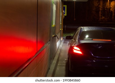 Car At The Fast Food Window. The Car Is In Line At The Auto Cafe. The Car Was Filmed From The Back At Night. Transport Stopped At Fast Food At Night.