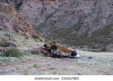 The car fell into the abyss and burned after the fall. The car after it burned down. Burnt car on the background of a rock.